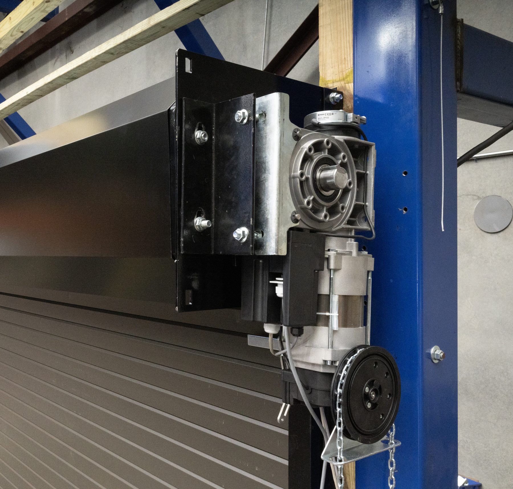 Gear-head operator and chain hoist mounted beside the hood of a rolling steel door