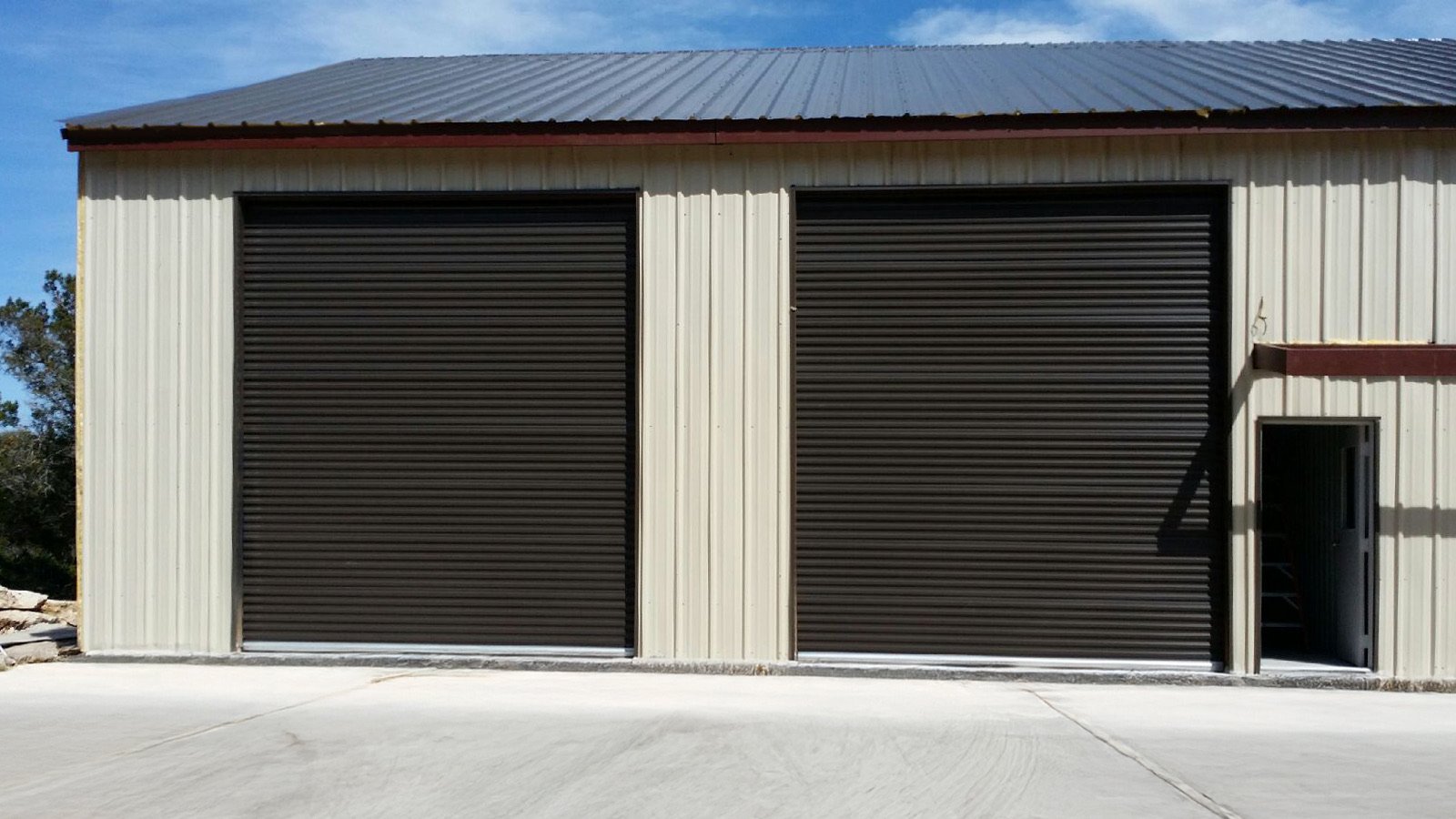 Janus Model 1100 roll-up doors in a dark finish on a tan steel building