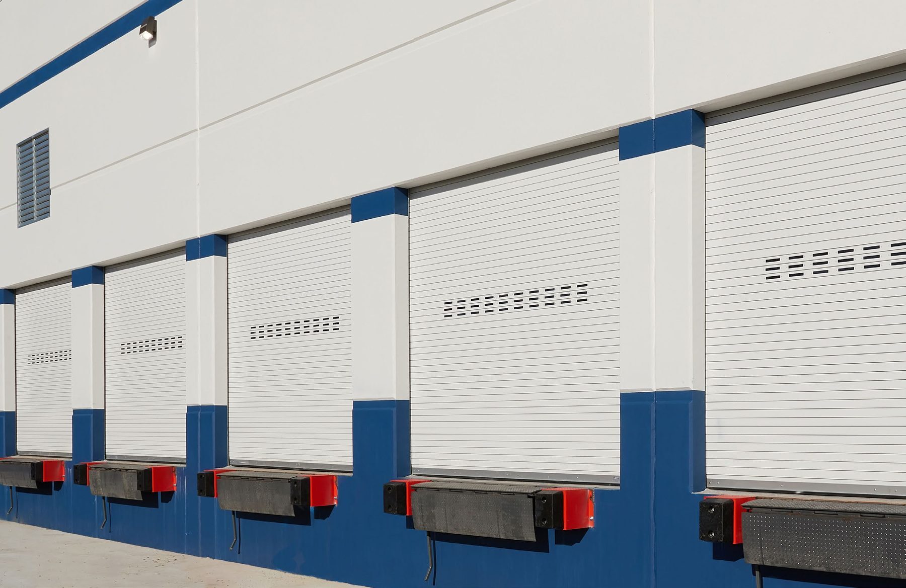 Row of white Janus rolling service doors with vision lites above dock levelers