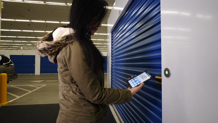 Woman accessing smart entry app on phone to open Janus door at self-storage unit.